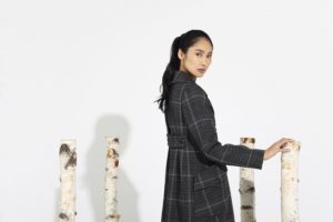 female model with ponytail wearing plaid coat, standing with birch tree pieces