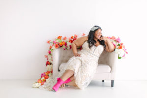 curvy black bride sitting on styled setee, wearing hot pink booties and curvy rose wedding gown