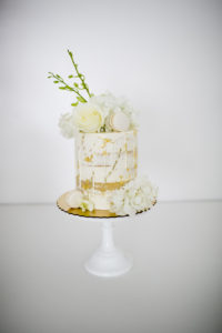 small white and gold cake with pale yellow roses and macarons