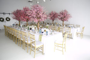 long white tables with gold chairs and cherry blossom centerpieces