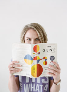 blonde woman peeking over The Gene book