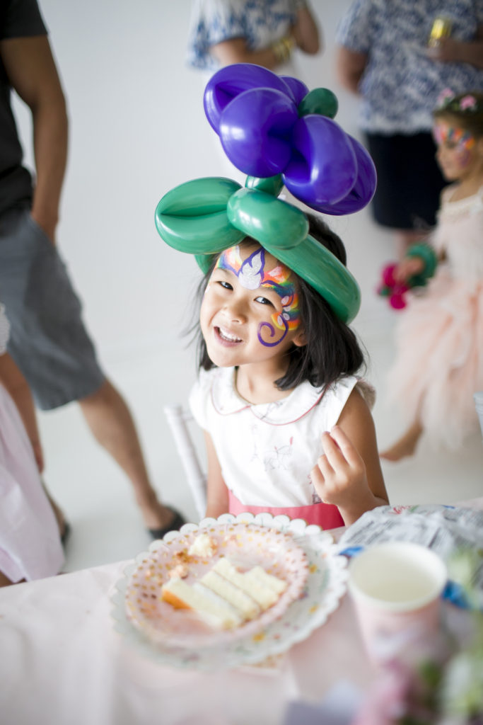 little girl with painted face wearing a balloon flower hat